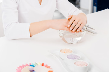 Obraz na płótnie Canvas Cropped shot of manicurist in white uniform sitting at workplace