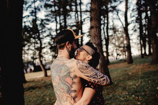 Young guy in tattoos hugging lady in forest
