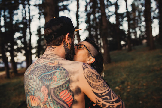 Young guy in tattoos hugging lady in forest