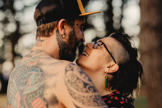Young guy in tattoos hugging lady in forest