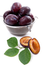 Steel colander with ripe plums, whole and half ripe plums with leaf isolated on a white background..