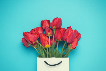 Bouquet of brightly red tulips in a white gift bag on a blue background. Conception of congratulations and a gift. Flat lay, top view