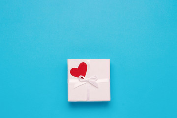 White gift box, red heart on a blue background. Minimalistic style. Concept surprise and suspense, a gift from a loved one. Flat lay, top view