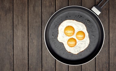 Three egg yolk on frying pan on wooden slats background