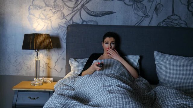 A beautiful Woman in bed being bored while zapping through the TV channels.
