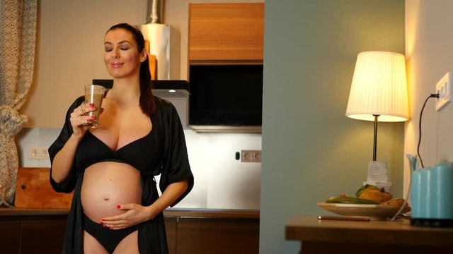 A beautiful pregnant woman in underwear having coffee in the kitchen at home.
