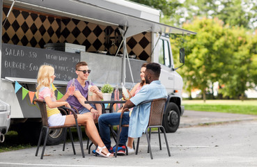 Fototapeta na wymiar leisure and people concept - happy friends with drinks sitting at table at food truck