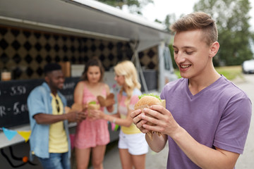 leisure, eating and people concept - happy man with hamburger and friends at food truck