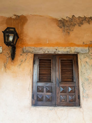 beautiful wooden window in mediterranean style in orange wet and molded old wall with metallic night lamp