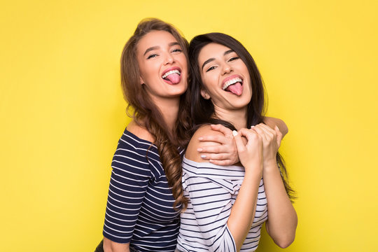 Lifestyle portrait of two pretty women showing tongue.