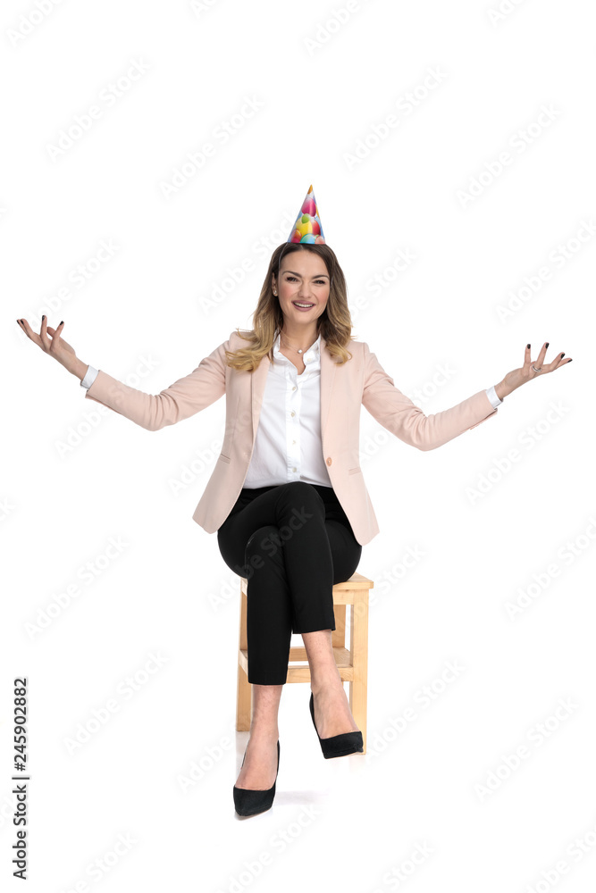 Sticker seated smart casual woman wearing birthday hat makes greeting gesture