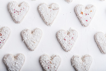 Fototapeta premium A pattern of Valentine's day white coconut heart shaped cookies on a white background with red sprinkles. Copy space. Monochrome