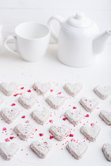  A pattern of Valentine's day white coconut heart shaped cookies on a white background  with red sprinkles. Copy space. Monochrome