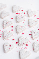  Valentine's day white coconut heart shaped cookies on a white plate with red sprinkles and white teapot. Copy space