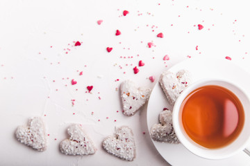  White tea cup with tea and Valentine's day white coconut heart shaped cookies with red and pink heart sprinkles. Copy space