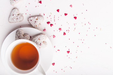  White tea cup with tea and Valentine's day white coconut heart shaped cookies with red and pink heart sprinkles. Copy space