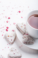 White tea cup with tea and Valentine's day white coconut heart shaped cookies with red and pink heart sprinkles. Copy space