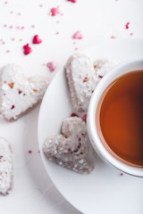  White tea cup with tea and Valentine's day white coconut heart shaped cookies with red and pink heart sprinkles. Copy space