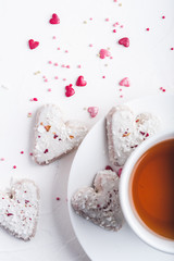  White tea cup with tea and Valentine's day white coconut heart shaped cookies with red and pink heart sprinkles. Copy space
