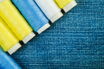 Spools of white, yellow and green  sewing thread arranged in row on denim with copy space