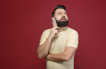 A cute and bearded brunette man on a red background says emotionally on the phone