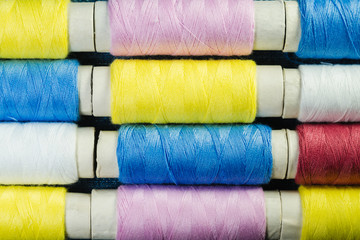 Spools of blue, yellow and pink  sewing thread arranged in rows on denim