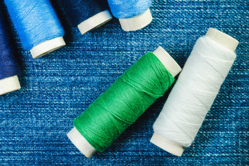Fototapeta na wymiar Spools of blue,white and green sewing thread on blue denim