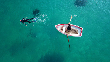Aerial drone bird's eye view of scuba diver near small traditional fishing boat in port of Mykonos in sapphire clear waters, Cyclades, Greece