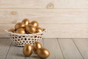 Happy easter! Easter eggs of golden color on a light wooden background.