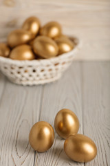 Happy easter! Easter eggs of golden color on a light wooden background.