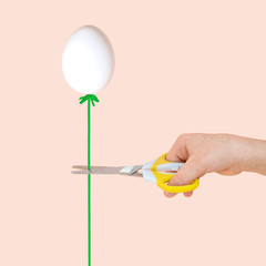 Female hand with scissors and egg like balloon