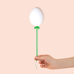 Female hand holding egg on ribbon like balloon
