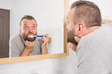 Fototapeta premium Bored guy brushing his teeth in bathroom