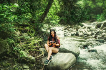 charming attractive dark-haired girl Sidin on the rocks near the cold clear mountain river in Martvili Canyon and reading a book on the gadget. perfect photo for advertising, peaceful paradise