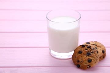 Glass of milk and chocolate cookies on pink background