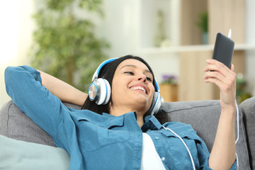 Happy woman on a couch listening to music at home