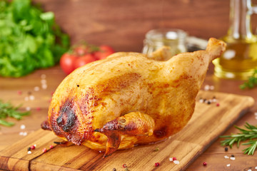 Whole roasted chicken on wooden cutting board on dark brown wooden table, side view
