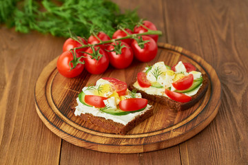 Smorrebrod - traditional Danish sandwiches. Black rye bread with boiled egg, cream cheese, cucumber, tomatoes on dark brown wooden background, side view