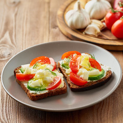 Smorrebrod - traditional Danish sandwiches. Black rye bread with boiled egg, cream cheese, cucumber, tomatoes on dark brown wooden background, side view