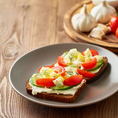 Smorrebrod - traditional Danish sandwiches. Black rye bread with boiled egg, cream cheese, cucumber, tomatoes on dark brown wooden background, side view