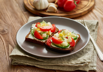Smorrebrod - traditional Danish sandwiches. Black rye bread with boiled egg, cream cheese, cucumber, tomatoes on dark brown wooden background, side view
