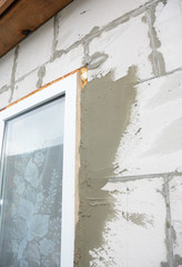 Plastering house wall with plastic window installation and insulation