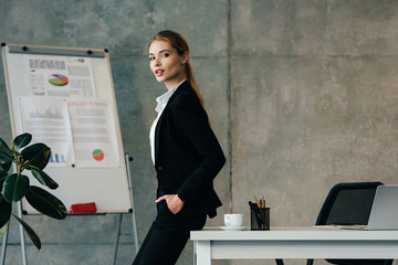 beautiful businesswoman standing by desk with hands in pockets