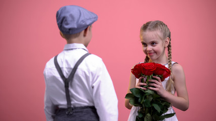 Young gentleman in formal clothes presenting roses bouquet to little female