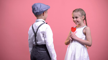Little boy gifting red heart-shaped lollipop to girlfriend, sweet romantic gift