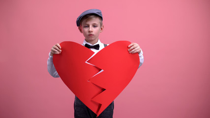 Sad male kid in vintage wear trying to fix broken paper heart, unrequited love