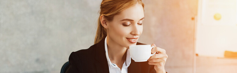 Charming businesswoman enjoys drinking coffee with closed eyes