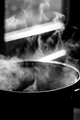the man stirs the soup in the pan from which steam comes