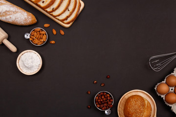 Homemade breads or bun, croissant and bakery ingredients, flour, almond nuts, hazelnuts, eggs on dark background, Bakery background frame, Cooking breakfast concept. Flat lay, Top view.