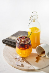 Ice cold summer drink. Orange juice espresso with ice, bottle of organic orange juice and empty espresso shot on white marble serving plate over white background. Copy space for text.